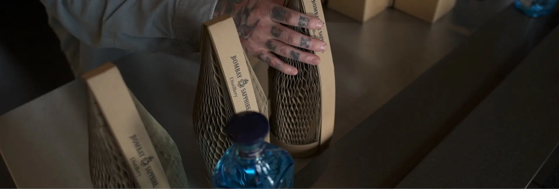 A man with tattoos on his hands picking up a bottle packed in Flexi-Hex slender premium plastic free packaging