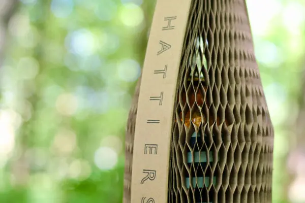 A bottle of Hattiers Rum inside Flexi-Hex protective slender packaging which is sustainable, plastic free and committed to carbon neutrality with a blurred out background of a forest