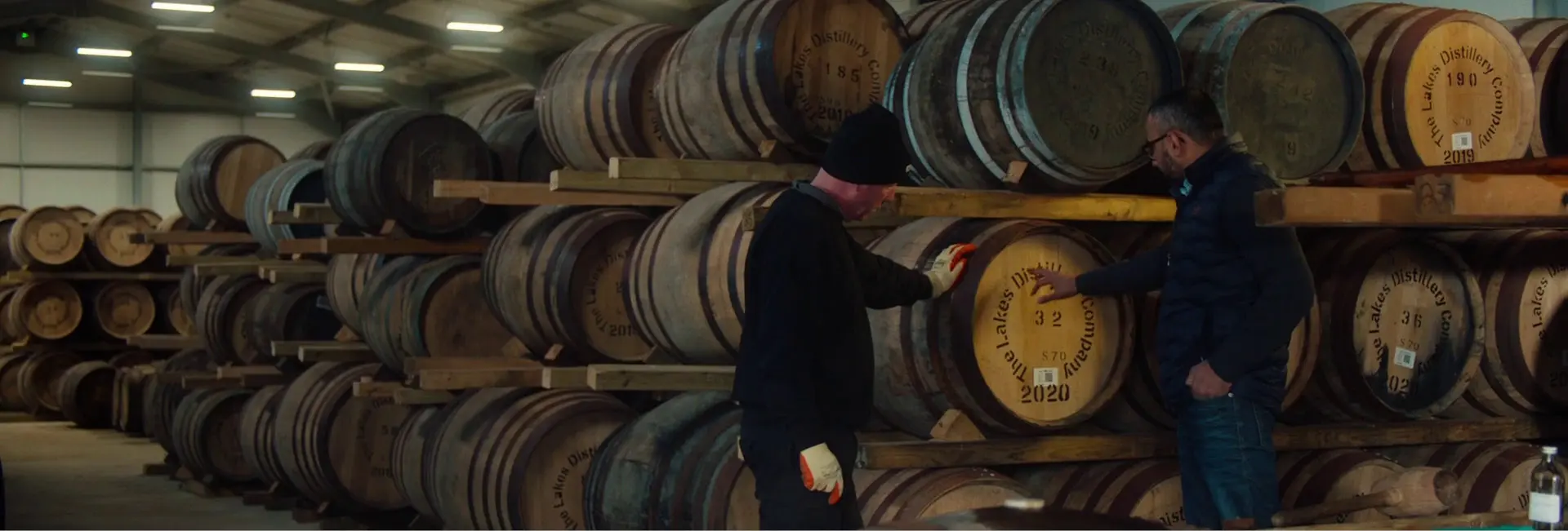 An image showing two men inspecting the oak barrels at The Lakes Distillery