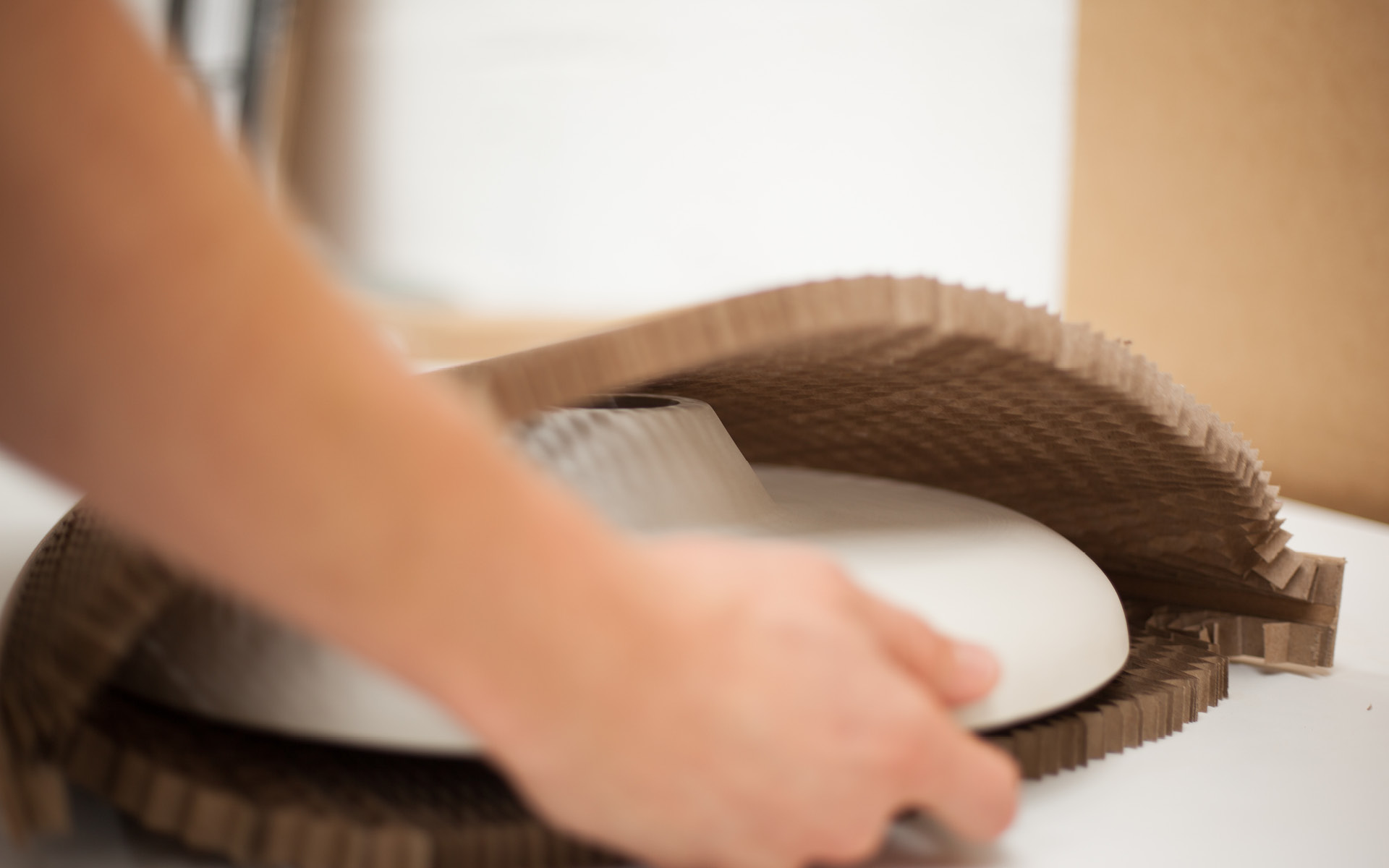 A person placing a bespoke hand made porcelain clay lampshade made by Studio Haran into a protective paper sleeve by Flexi-Hex